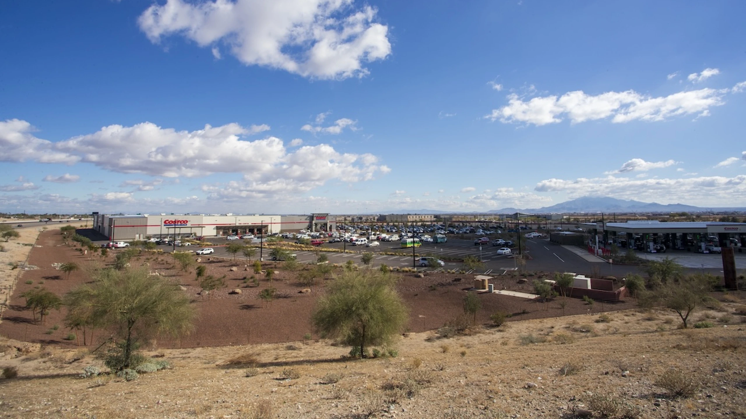 Aerial view of the Costco warehouse at Buckeye Commons with a large parking lot and fuel station, desert landscape and mountains in the background