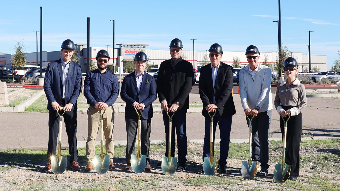 Seven people in SIHI-branded hard hats hold ceremonial gold shovels at a groundbreaking event with a Costco warehouse sign visible behind them