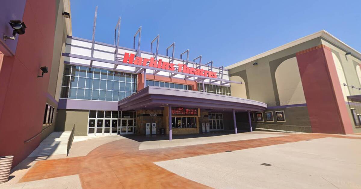 Exterior of a Harkins Theatres multiplex showing red branded signage above a covered purple-columned entryway with ticket windows against a blue sky.