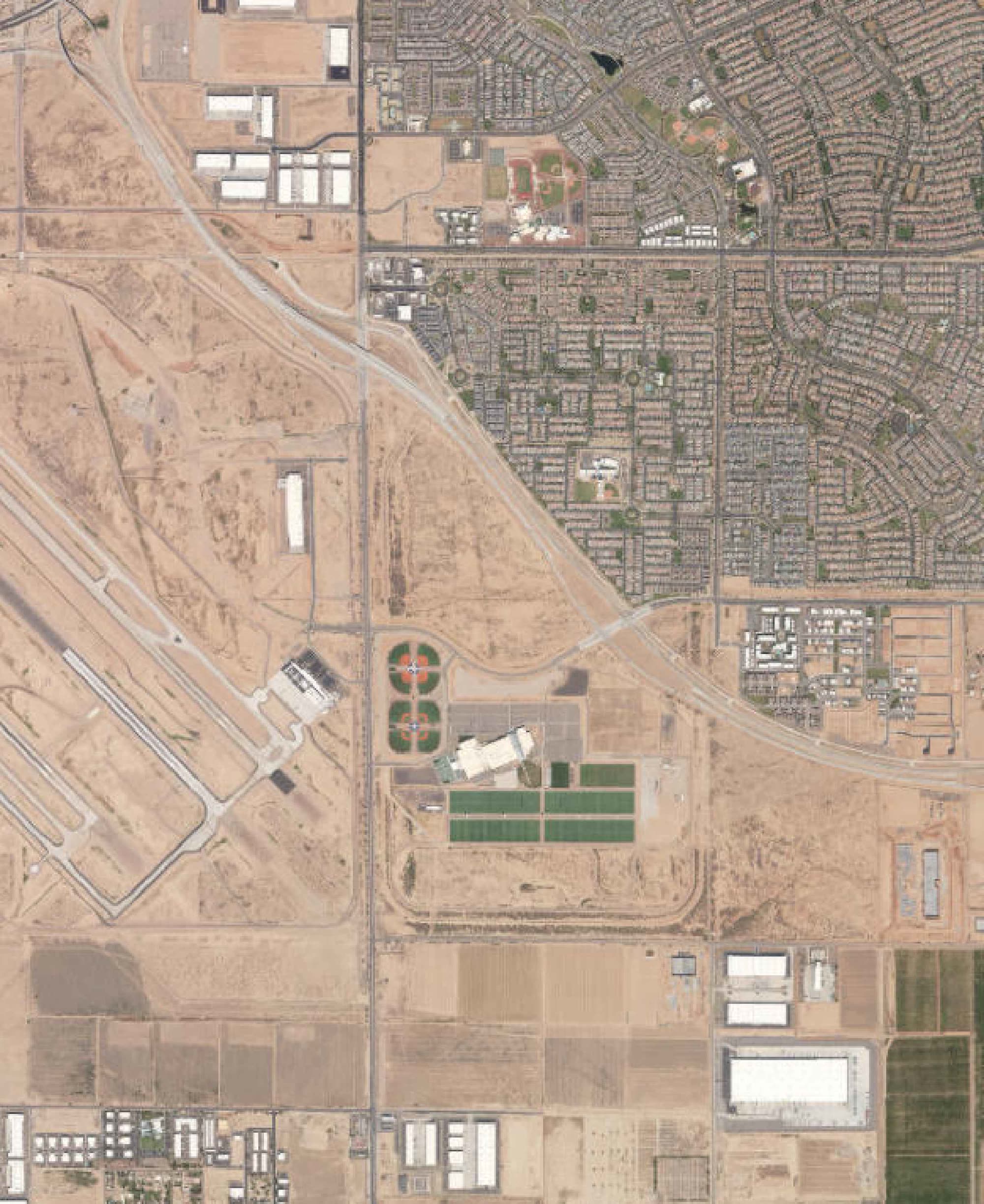 Satellite aerial view of the southeast Mesa area showing Phoenix-Mesa Gateway Airport runways at left, Arizona Athletic Grounds sports fields at center, suburban residential grid at upper right, and undeveloped desert parcels in the foreground near the Legacy Park site