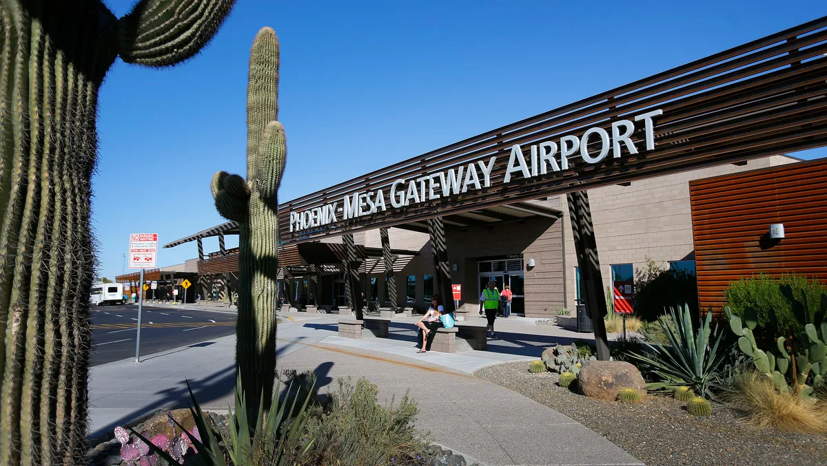 The exterior entrance of Phoenix-Mesa Gateway Airport with large lettering on the terminal canopy, saguaro cacti, and desert landscaping under a clear blue sky