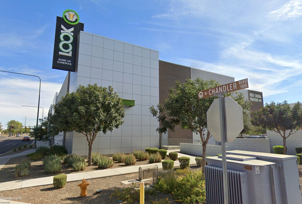 Street-level exterior photo of the LOOK Dine-In Cinemas building on W Chandler Blvd showing the tall black branded sign with green logo, modern grey panel facade, desert landscaping, and a street sign in the foreground.