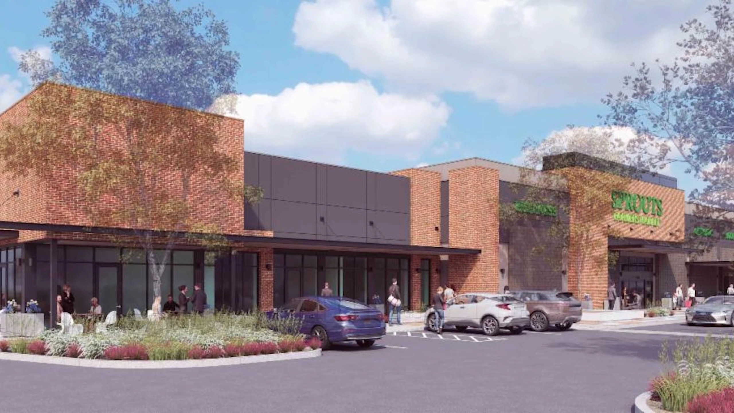 Architectural rendering of Eastmarket at Eastmark showing a strip retail center with brick and dark panel facades, a Sprouts Farmers Market sign on the right anchor unit, shoppers, and parked cars in the foreground.