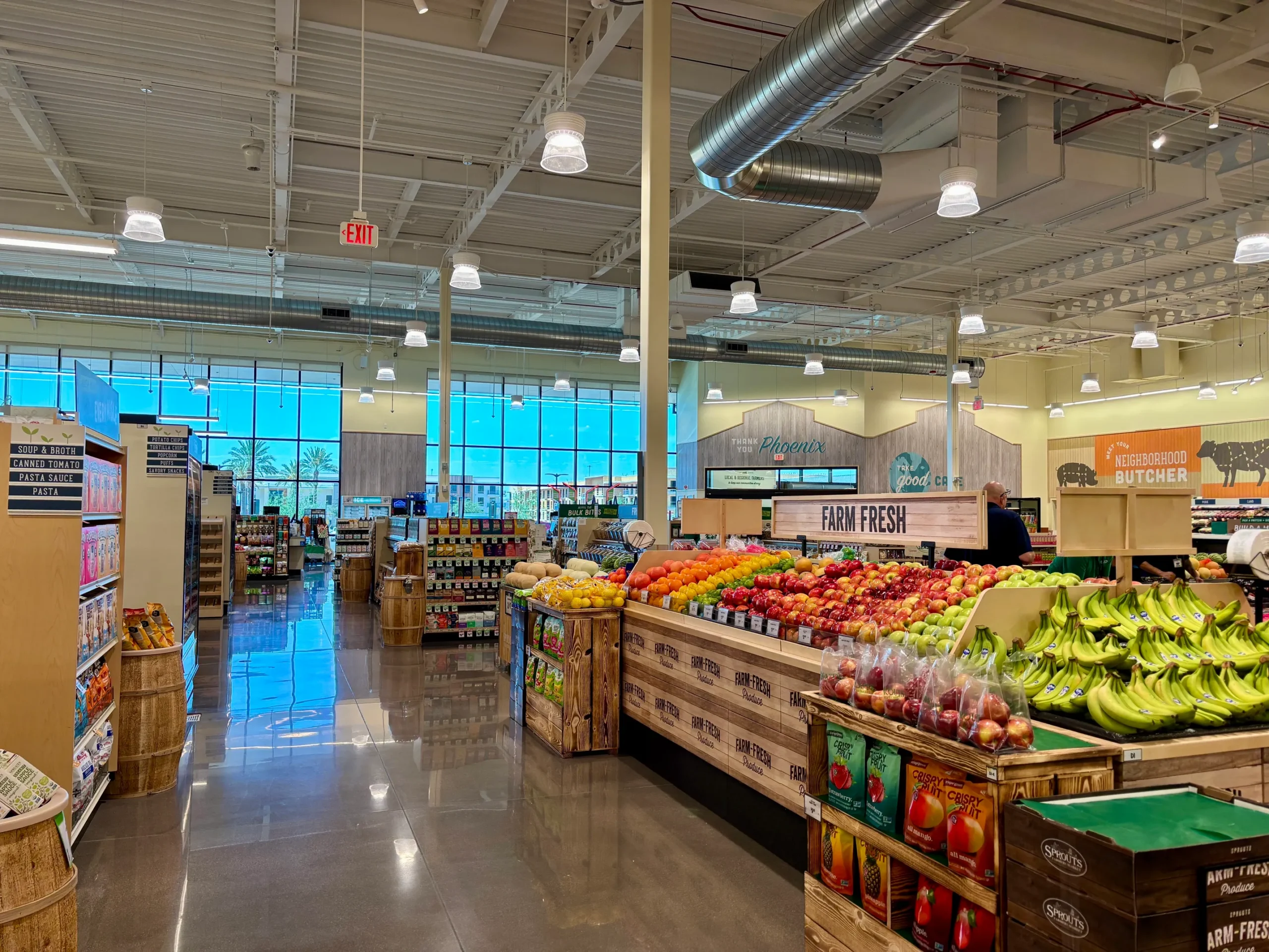 Interior of a Sprouts Farmers Market showing fresh produce in wooden bins and grocery aisles extending toward large front windows