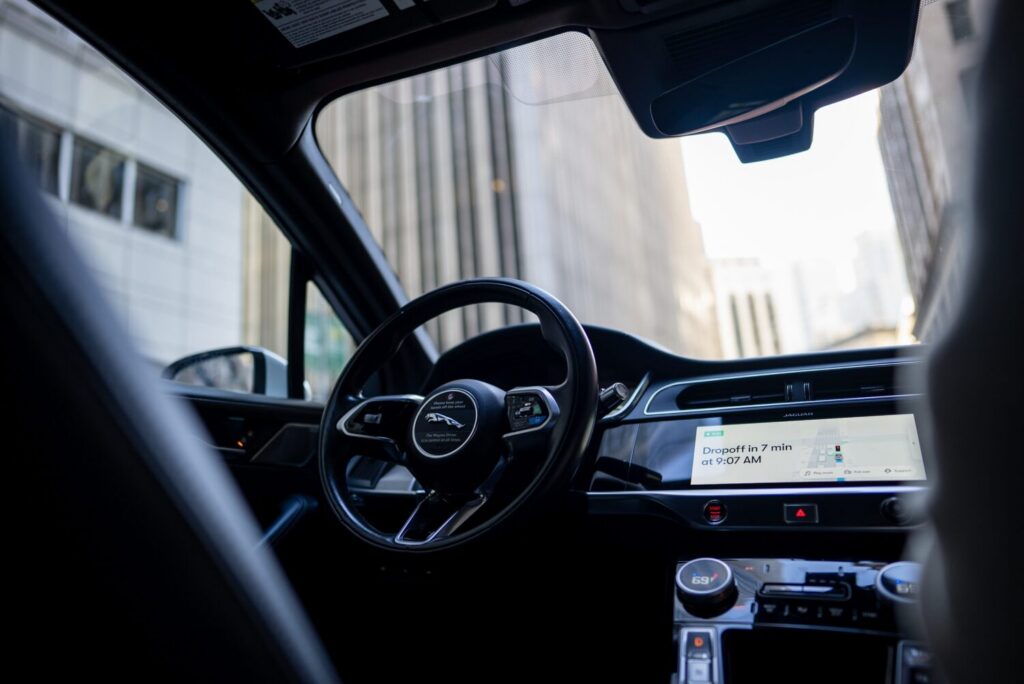 Interior of a Waymo autonomous Jaguar I-PACE robotaxi showing the Waymo-branded steering wheel and an infotainment screen displaying dropoff navigation information